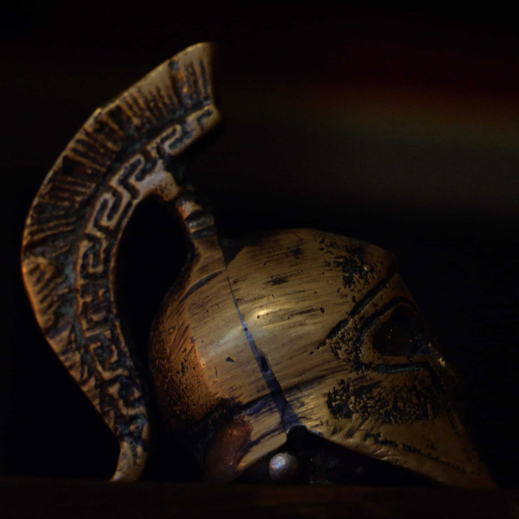 Casque Spartiate en Bronze | Grèce Antique & Guerriers Réplique détaillée d'un casque spartiate en bronze patiné, orné d'un motif de méandre grec sur la crête, sur un fond sombre.